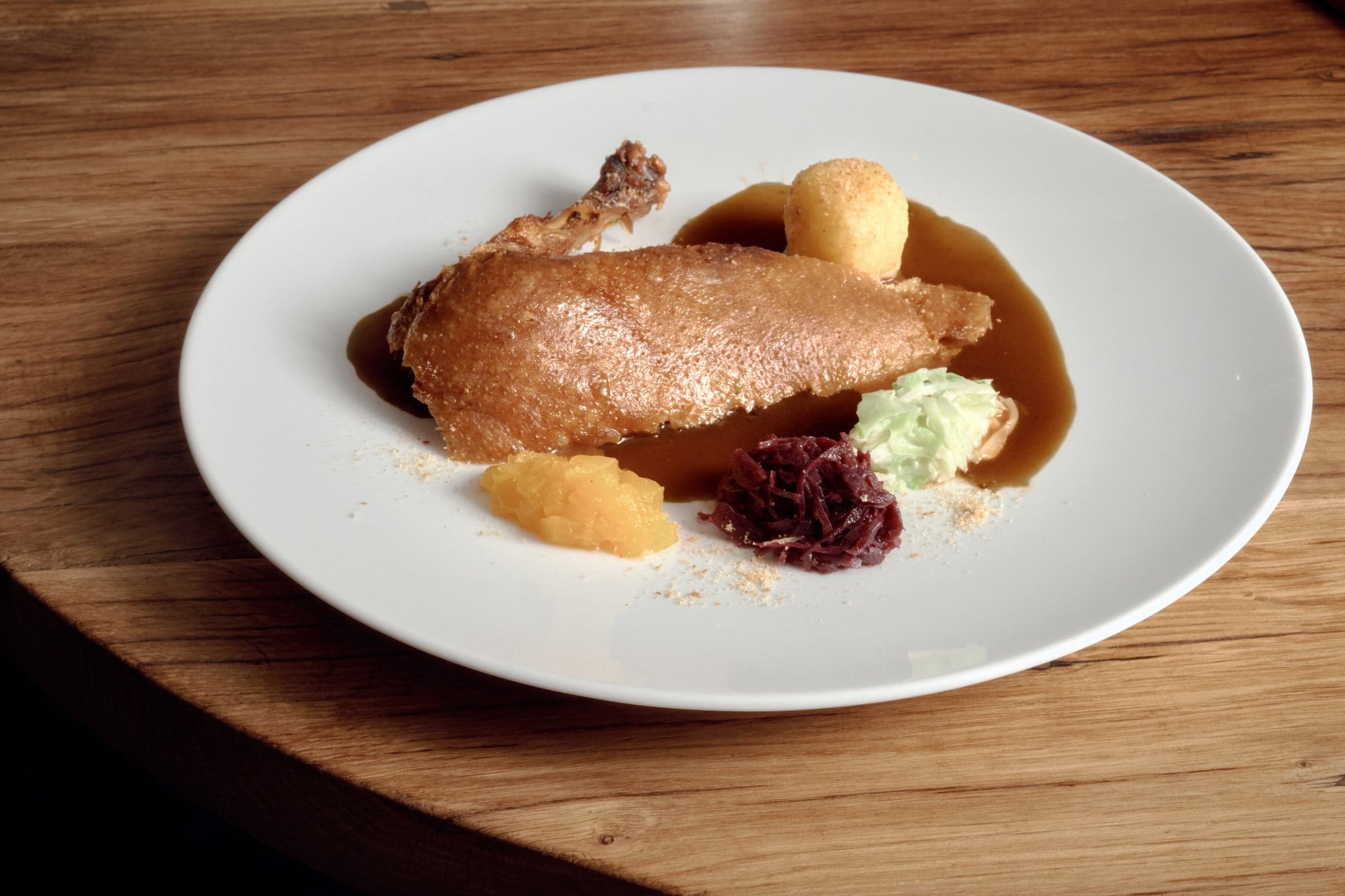 The duck on the plate with potato dumpling, red cabbage, savoy cabbage, apple compote and jus