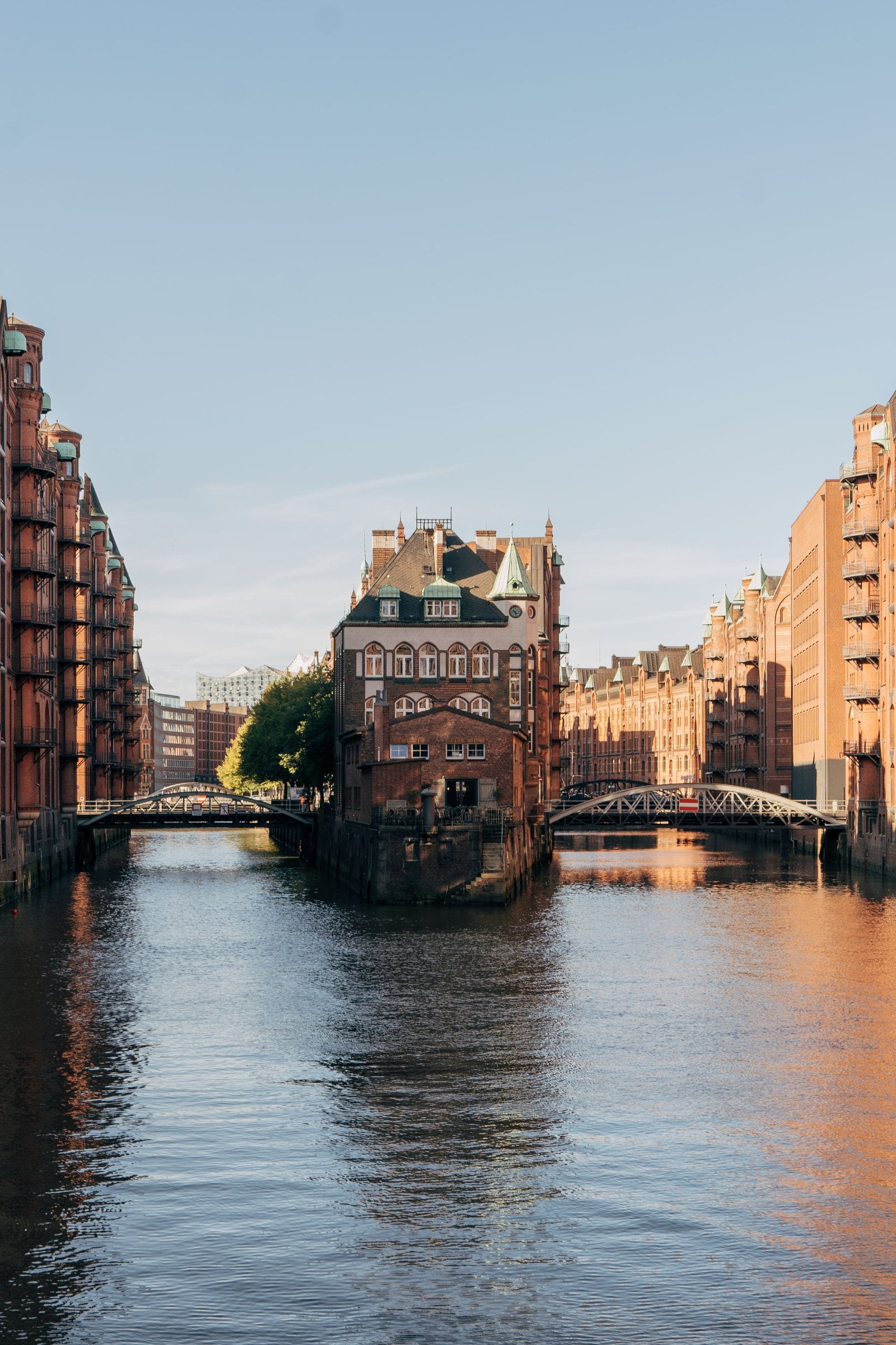 The Speicherstadt by the water with the Wasserschloss between two bridges, the Elbphilharmonie in the background